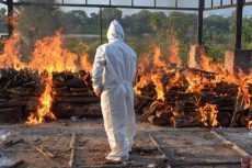 A frontline worker setting fire to funeral pyres at a cremation site.